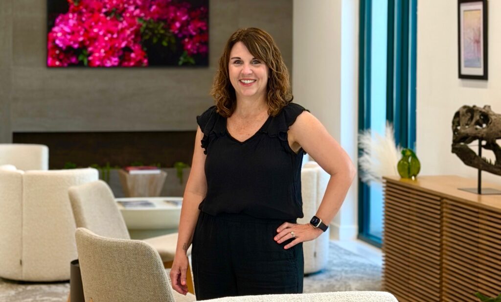 Diane Womble, team member at Premier Prosthodontics in Raleigh, standing and smiling in the comfortable patient waiting area.