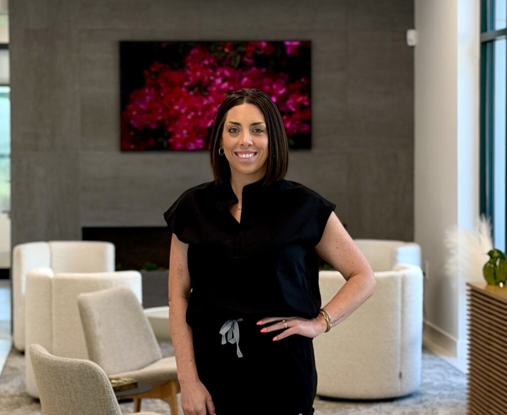 Sarah Zeback of Premier Prosthodontics in Raleigh wearing black scrubs and smiling in the clinic lobby.