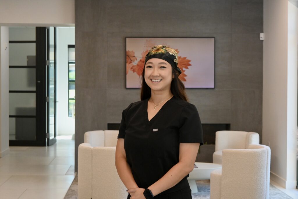 Trina Tran from Premier Prosthodontics posing playfully in black scrubs in the clinic's waiting area.